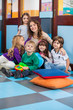 Teacher And Students Sitting On Floor In Classroom