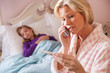Mother reads thermometer while daughter sick in bed.