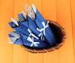 Forks and knives wrapped in blue paper napkins, in basket,