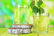 Glasses of birch sap on wooden table, on green background