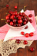 Ripe red cherry berries in bowl on wooden table close-up