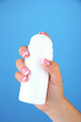 Woman hand holding bottle with cream on color background