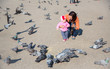 Photo: Child girl and mum playing with doves in the city street Child girl and mum playing with doves in the city street