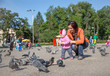 Photo: Child girl and mum playing with doves in the city street Child girl and mum playing with doves in the city street