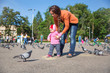 Photo: Child girl and mum playing with doves in the city street Child girl and mum playing with doves in the city street