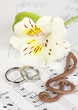 Treble clef, flower and wedding rings on musical background