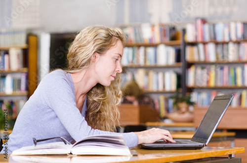 Photo: female student with laptop working in library female student with laptop working in library
