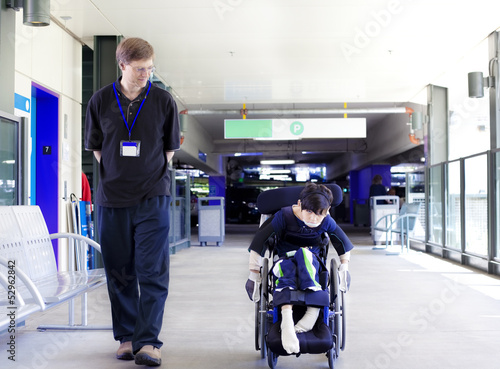 Photo: Father walking with disabled son in wheelchair to the hospital Father walking with disabled son in wheelchair to the hospital