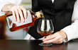 Barman hand with bottle of cognac  pouring drink into glass,