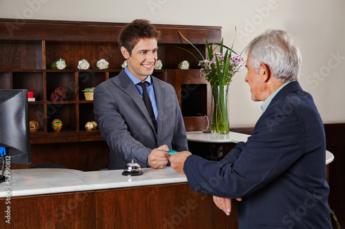 Photo: Rezeptionist im Hotel gibt Senior Schlüsselkarte Rezeptionist im Hotel gibt Senior Schlüsselkarte