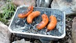 sausages cooking on a disposable barbecue outdoors