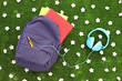 School backpack with books and headphones on a grass with daisy