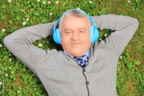 Photo: Mature man lying on grass with headphones, listening to music Mature man lying on grass with headphones, listening to music