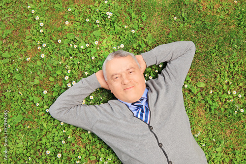 Photo: Senior man smiling and resting on grass in a park Senior man smiling and resting on grass in a park