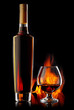 Foto: Bottle and glass of cognac over dark background with flame Bottle and glass of cognac over dark background with flame