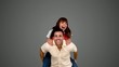Smiling man giving to his friend a piggyback on grey background