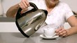 Woman pouring hot water from kettle into cup