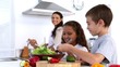 Siblings making salad together with mother watching