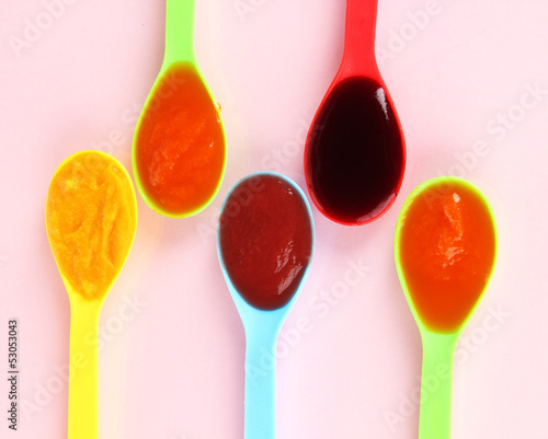 Photo: Baby puree in spoons on pink background Baby puree in spoons on pink background