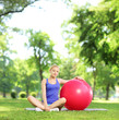 Blond female in sportswear sitting on a grass with pilates ball