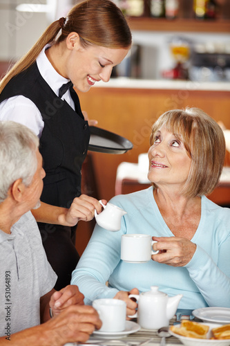 Photo: Kellnerin schenkt Seniorin Milch in den Kaffee Kellnerin schenkt Seniorin Milch in den Kaffee