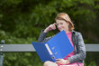 young female student with file seated on a bench, outdoors