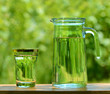 A Glass and а Carafe Full of Water on the Background of Foliage