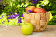 Basket with apples on stone surface over beautiful flower garden