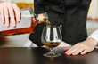 Barman hand with bottle of cognac  pouring drink into glass,