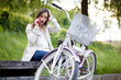Young woman sitting on the bench next to her bike talking on the