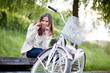 Young woman sitting on the bench next to her bike and talking on