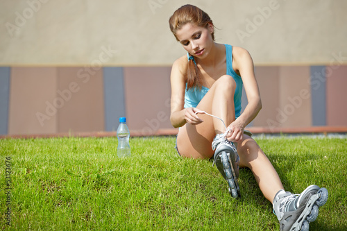 Photo: Woman skating in city. Girl going rollerblading sitting in grass Woman skating in city. Girl going rollerblading sitting in grass
