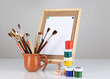 Small easel with sheet of paper and art supplies isolated
