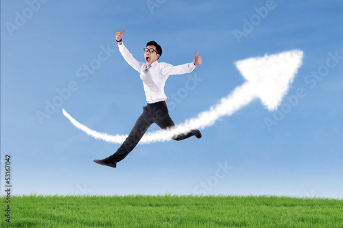 Photo: Asian businessman jumping over up arrow sign cloud Asian businessman jumping over up arrow sign cloud