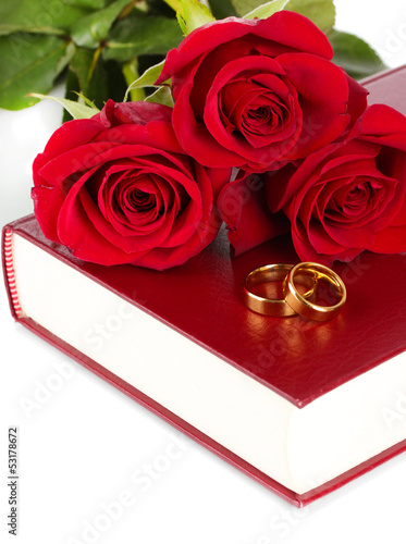 Photo: Wedding rings with roses on bible isolated on white Wedding rings with roses on bible isolated on white