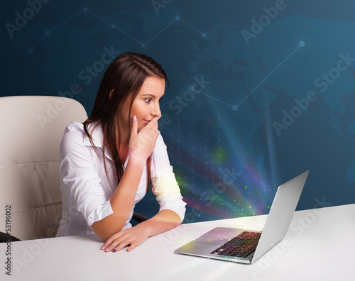 Photo: Beautiful woman sitting at desk and typing on laptop with abstra Beautiful woman sitting at desk and typing on laptop with abstra