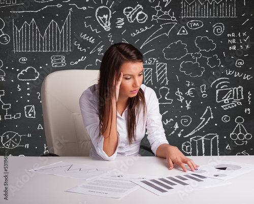 Photo: Businesswoman sitting at desk with business scheme and icons Businesswoman sitting at desk with business scheme and icons