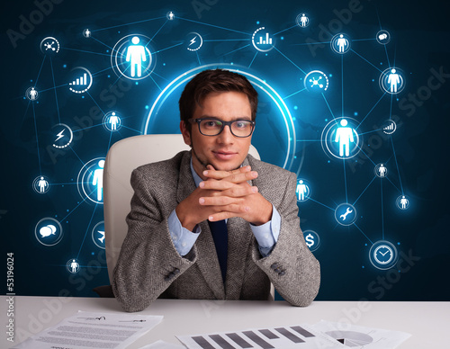 Photo: Businessman sitting at desk with social network icons Businessman sitting at desk with social network icons