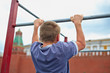 Boy does chin-ups against kremlin wall, back view