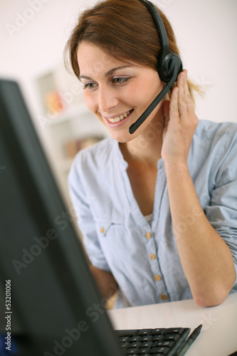 Photo: Young woman at work talking on phone with headset Young woman at work talking on phone with headset
