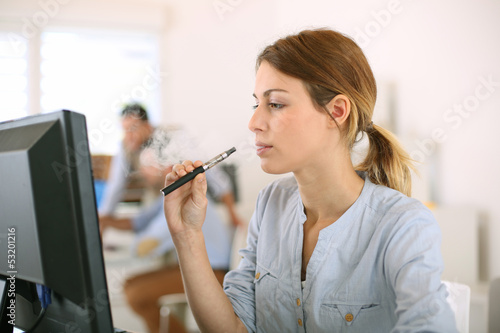 Photo: Girl smoking with electronic cigarette in office Girl smoking with electronic cigarette in office