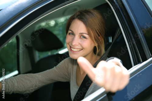 Photo: Cheerful girl sitting inside car with thumb up Cheerful girl sitting inside car with thumb up