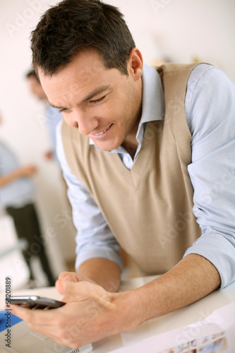 Photo: Man in office sending message with smartphone Man in office sending message with smartphone