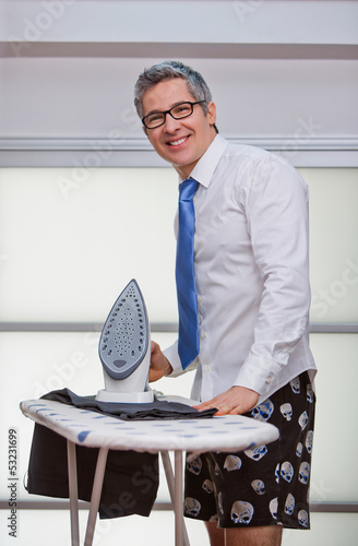 Photo: Portrait of a businessman smiling while ironing pants Portrait of a businessman smiling while ironing pants