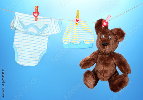 Photo: Baby clothes hanging on clothesline, on blue background Baby clothes hanging on clothesline, on blue background