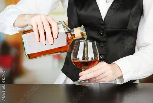 Photo: Barman hand with bottle of cognac pouring drink into glass, Barman hand with bottle of cognac pouring drink into glass,
