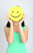 Young woman holding paper with happy smiley on gray background.