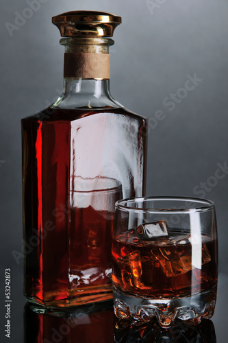 Photo: Brandy glass with ice and bottle on grey background Brandy glass with ice and bottle on grey background