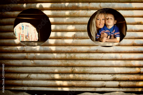 Photo: Mother and son peeks through hole at playground Mother and son peeks through hole at playground