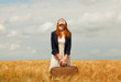 Redhead girl with suitcase at spring wheat field.
